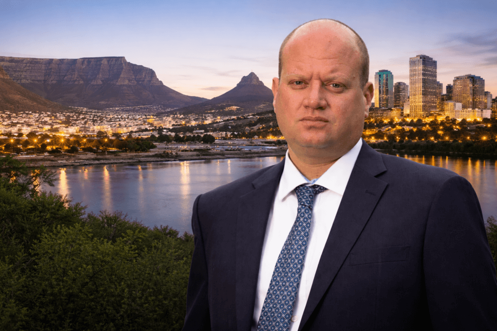 Professional portrait of Rory Ziv in a navy suit and patterned tie standing before a blended backdrop of Cape Town’s Table Mountain and Edmonton’s downtown skyline at dusk, symbolizing his journey from South Africa to Alberta.